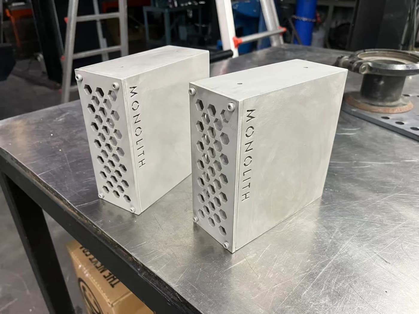 Original workshop photograph of two physical aluminium Monolith enclosure prototypes with honeycomb front panels